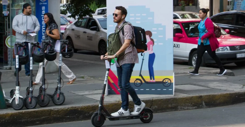 Usuario de scooter eléctrico en la CDMX, con más unidades de renta estacionadas en la acera, dentro del nuevo marco de regulación de movilidad.